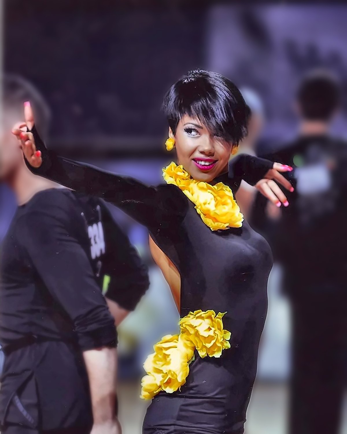 Raliza Velichkova on the competition floor in a black Latin dress with yellow flowers, one hand raised